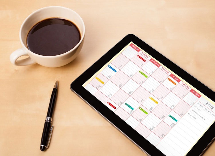 Calendar on ipad next to coffee and pen